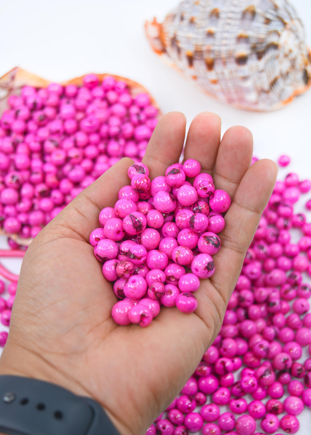 Close-up detail of pink acai beads for jewelry making, details of black marking of the natural beads in the hands.