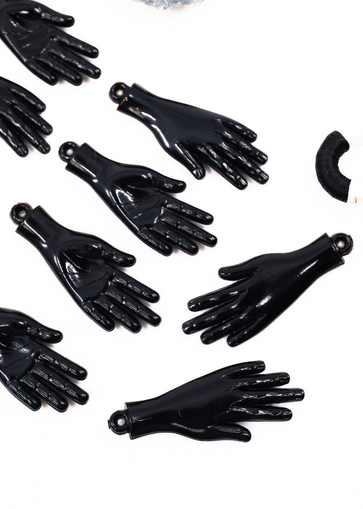 Several glossy black hand-shaped charms or pendants arranged on a plain white background. Made from German resin.