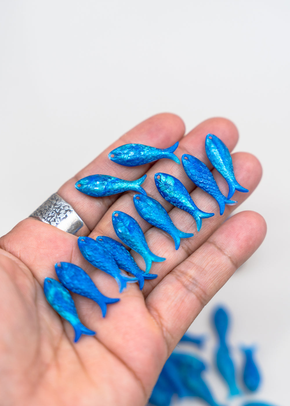 A hand holding several small glittery blue fish-shaped charms or beads against a plain light background.