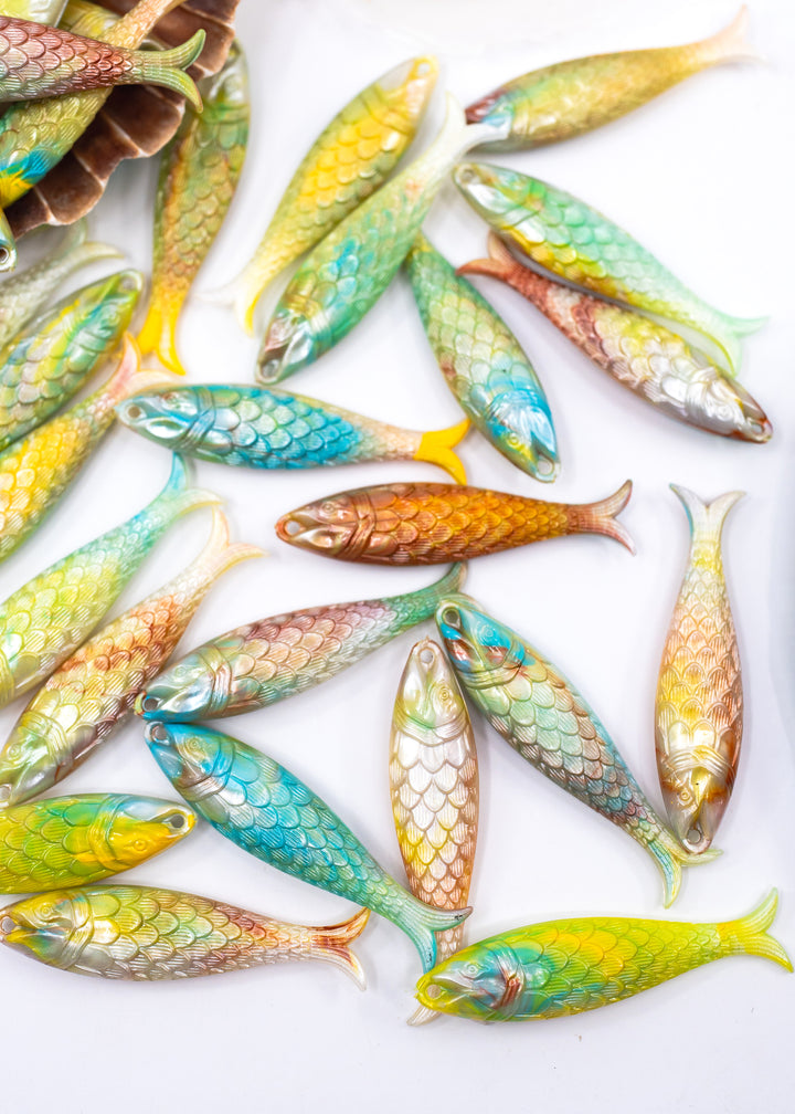 A collection of small, colorful fish-shaped items with detailed scales, arranged on a plain white background. Sold by nature Beads, made from German resin, beautiful fish charms.