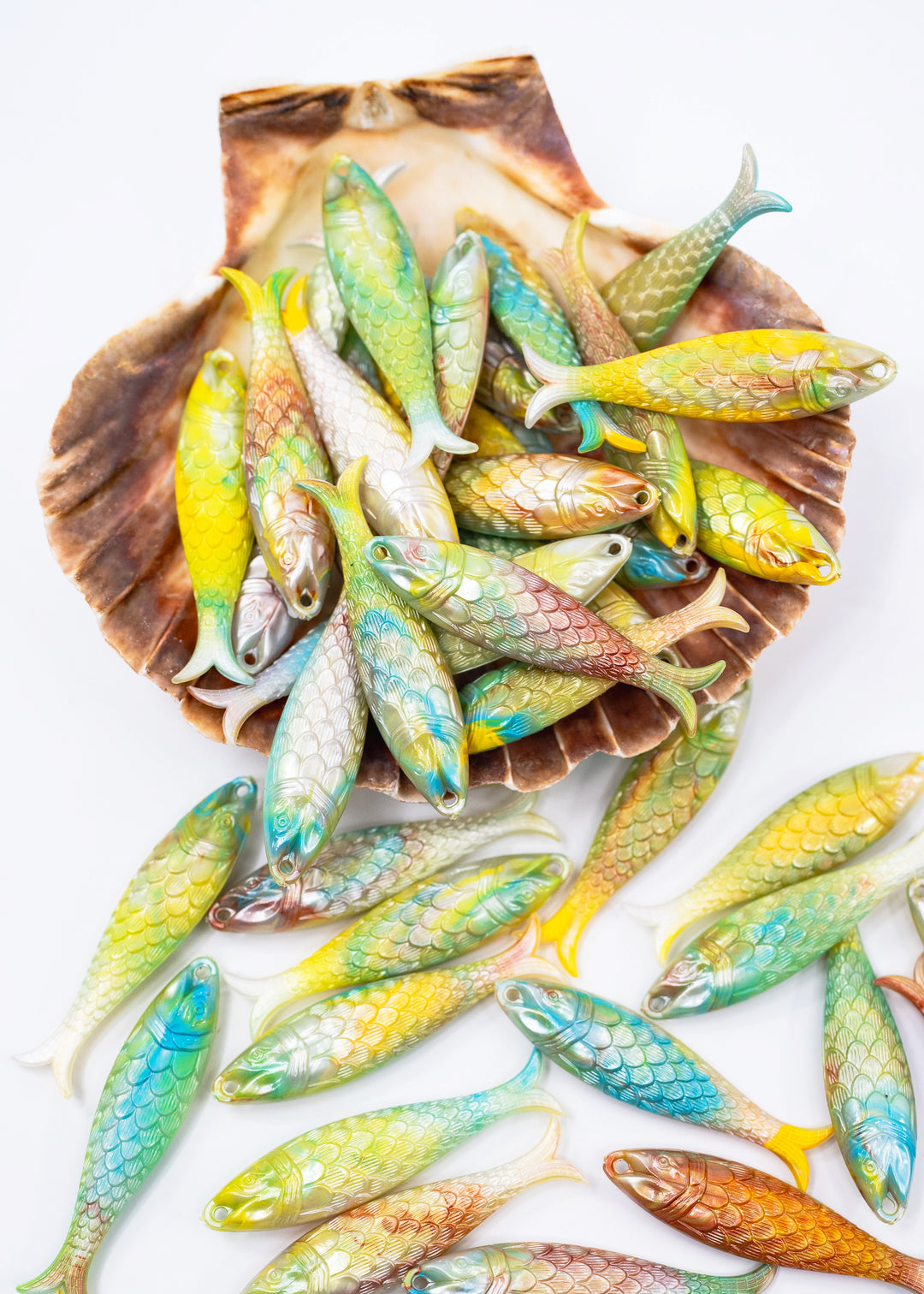 A collection of small, colorful fish-shaped ornaments or beads arranged inside and around a brown shell on a plain white background. Sold by nature Beads, made in German from vintage molds.