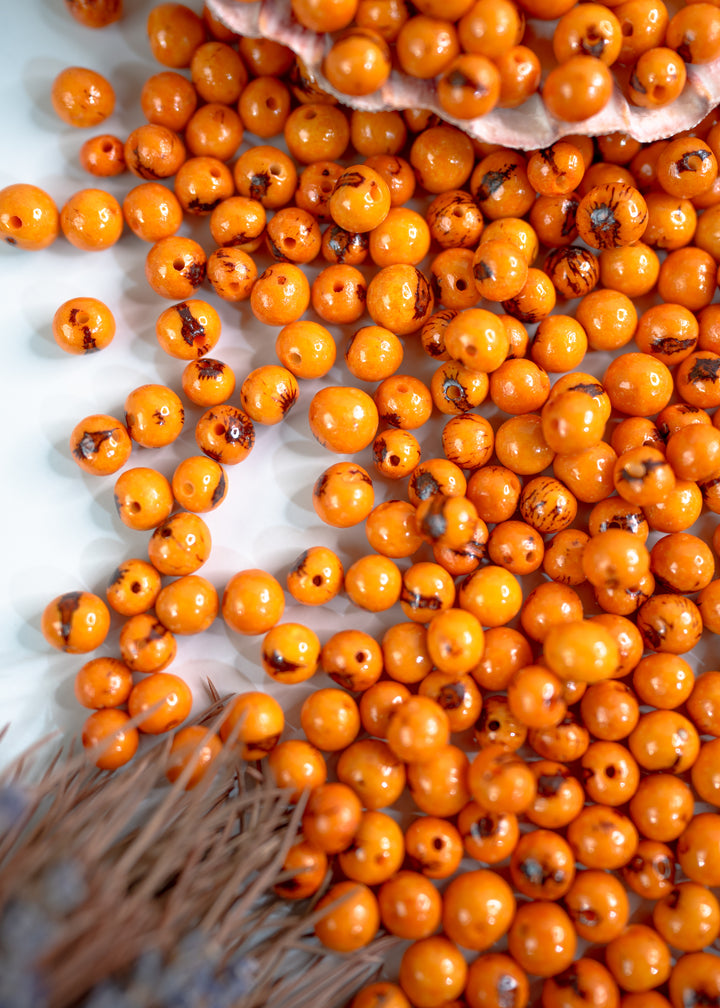 Assortment of natural acai beads in orange showing the natural black markings.