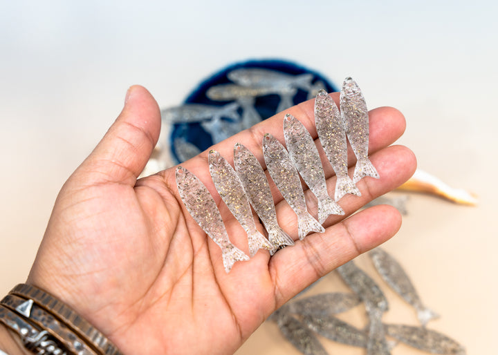 A hand holding several small glittery fish-shaped accessories. Made from German resin fish charms for jewelry making.