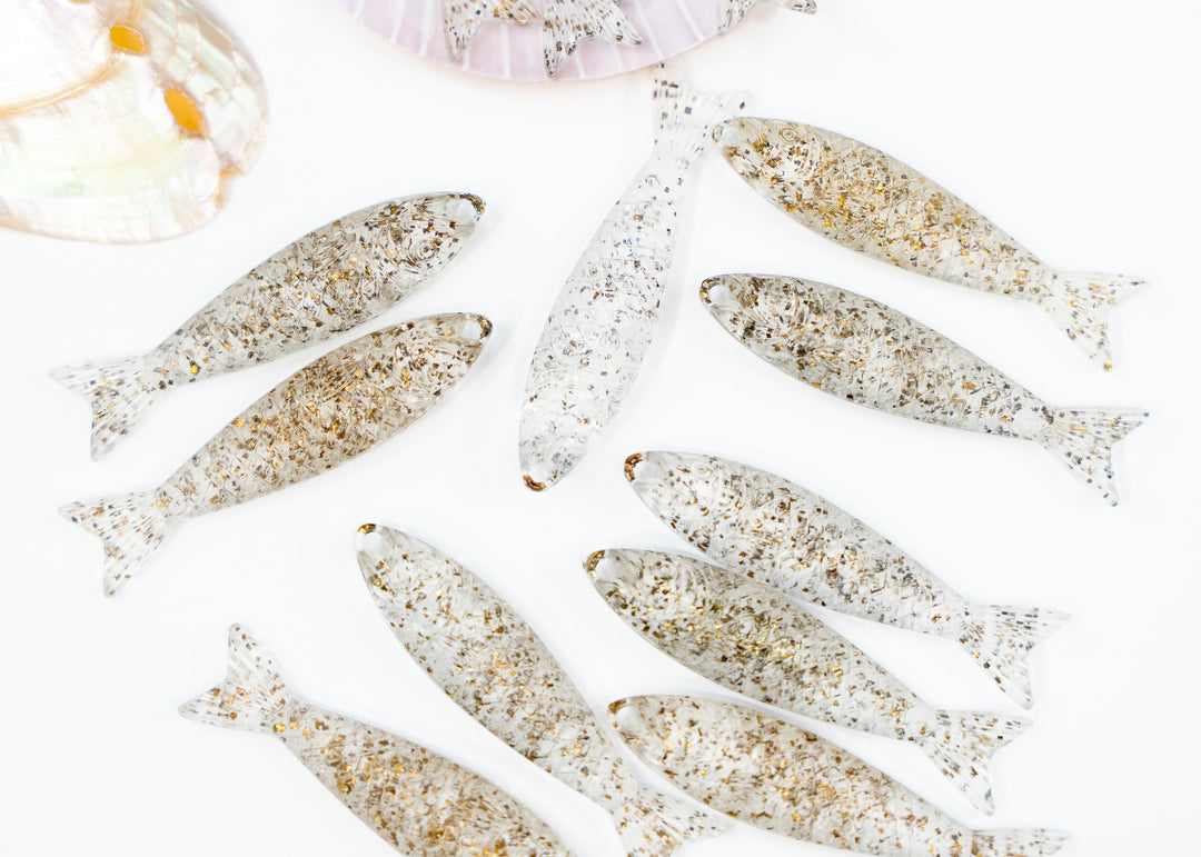 A set of small fish-shaped ornaments or charms with a speckled white and gold pattern fish charms made from German resin for jewelry making.