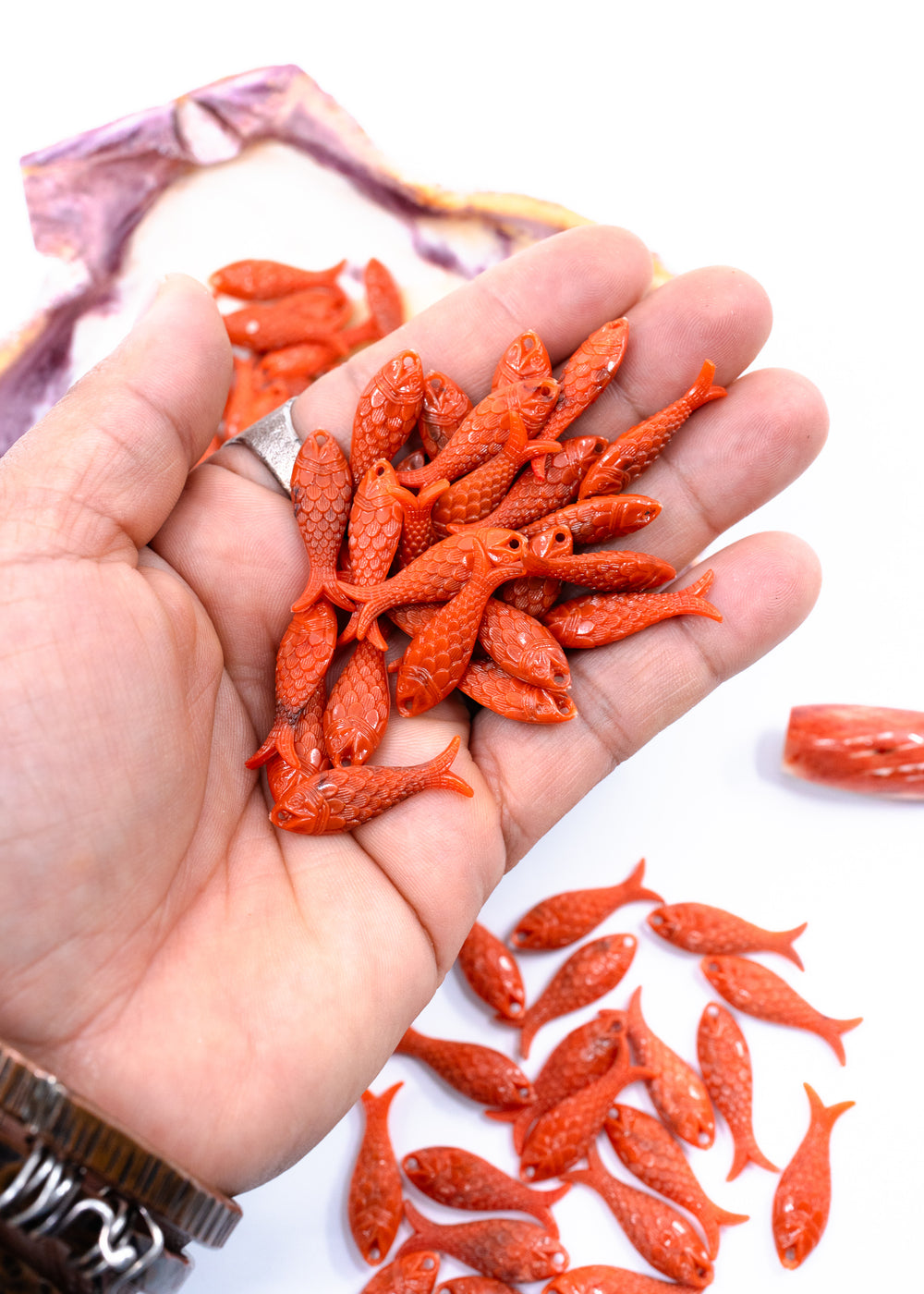 A hand holding several small orange-red fish-shaped beads. 