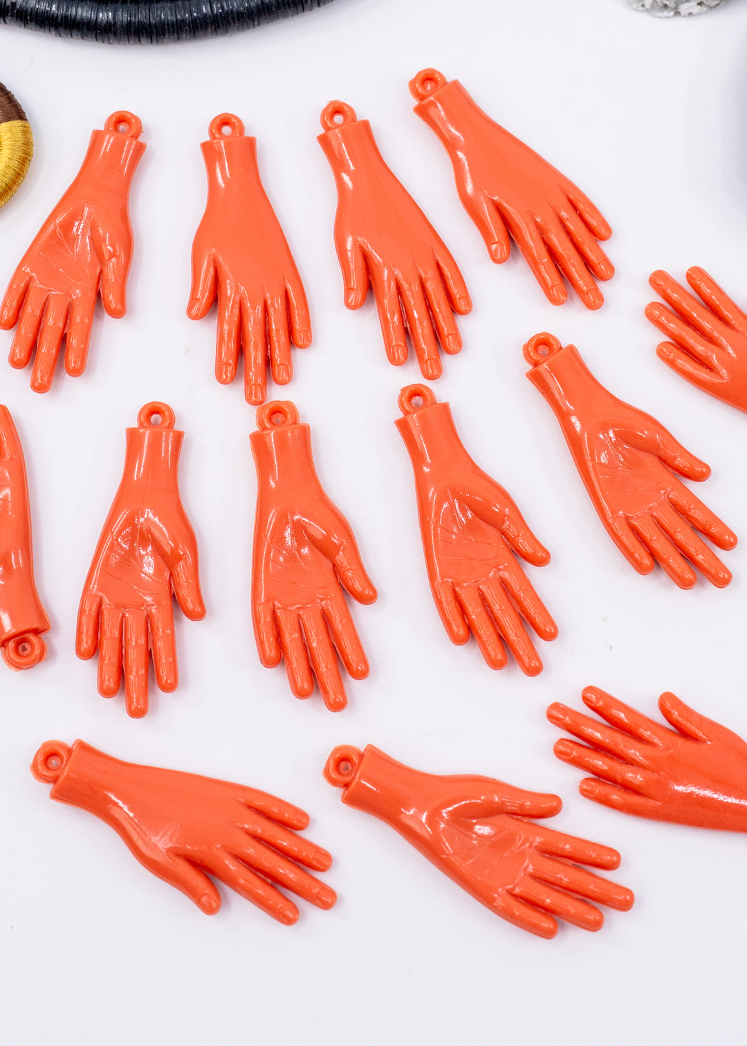Multiple small glossy orange hand-shaped charms or pendants arranged on a plain white background. Made from German resin.