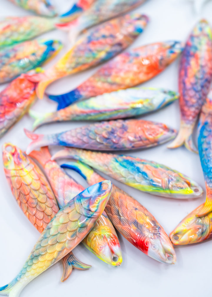 A pile of small, colorful German resin fish-shaped items with detailed scales and painted patterns in orange, blue, yellow, and red on a white background.