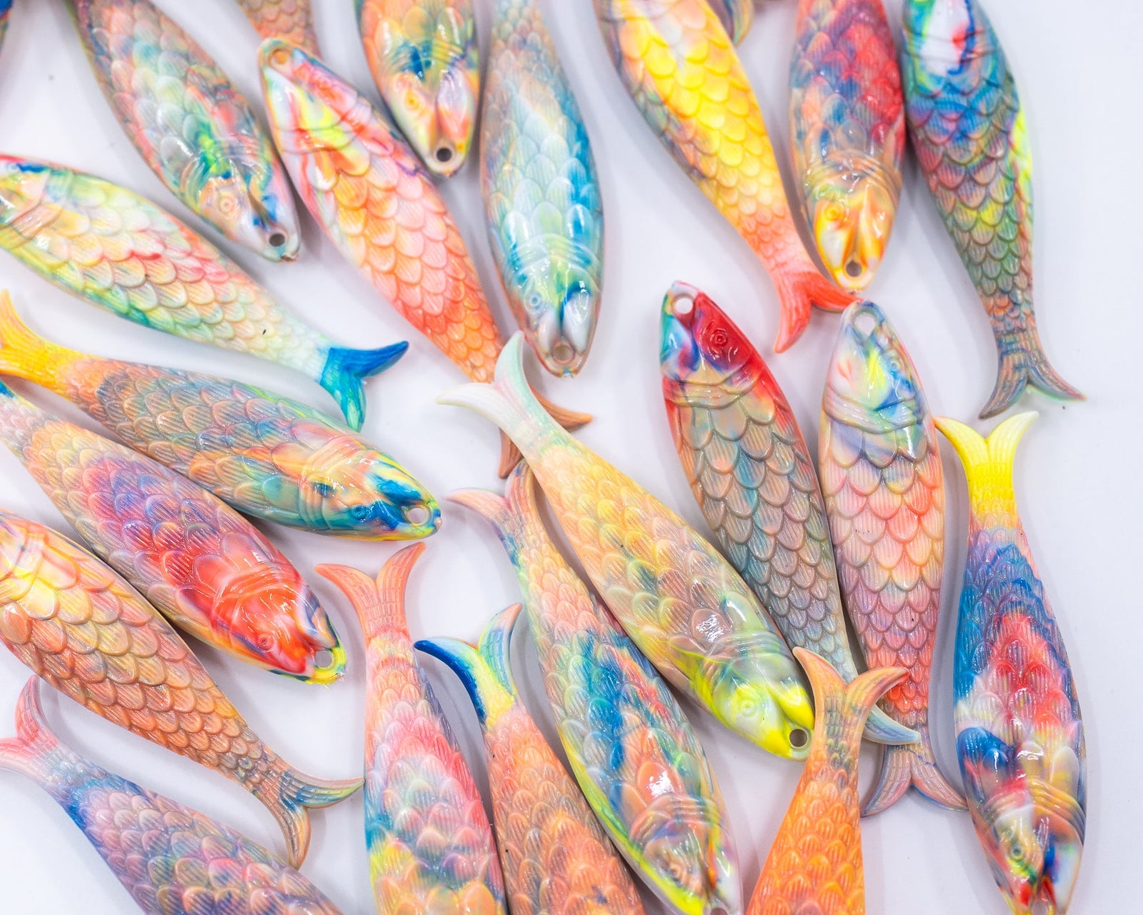 A collection of colorful, fish-shaped German resin charms with detailed scales, painted in vibrant shades of orange, yellow, blue, red, and green, arranged on a white background.