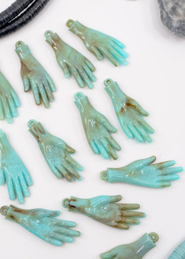 Multiple turquoise and green marbled hand-shaped jewelry charms scattered on a white background, made from German resin.