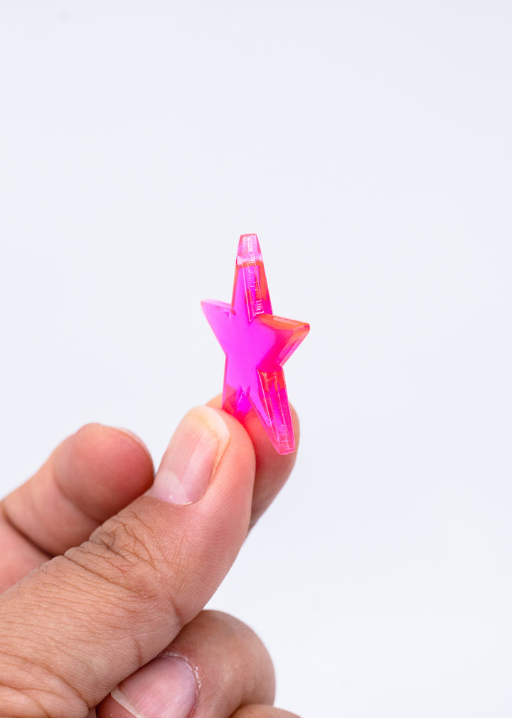 A hand holding a small, translucent hot pink star-shaped object against a plain white background, made from German resin.