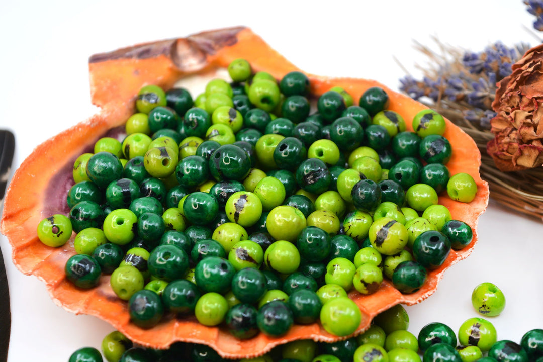 Natural Acai Beads in two different shades of green displayed in a seashell.