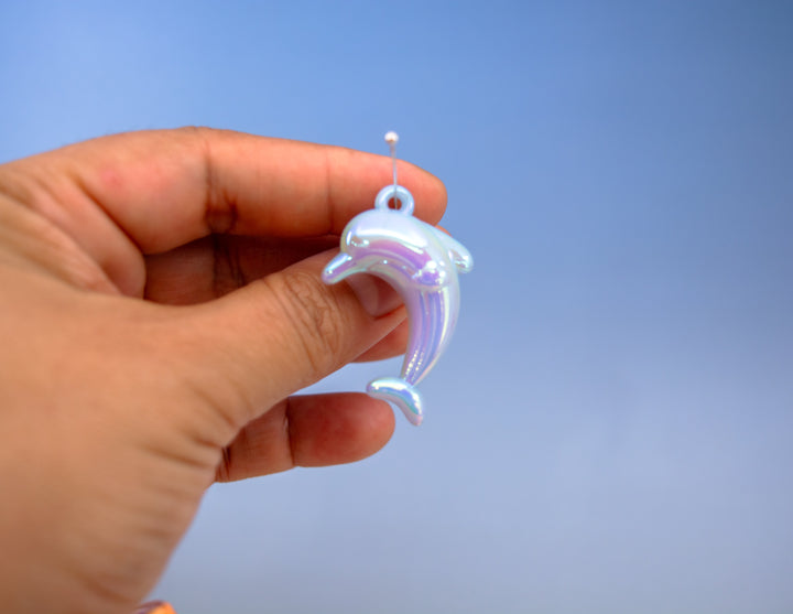 A hand holding a small iridescent dolphin-shaped pendant or charm for jewelry making.