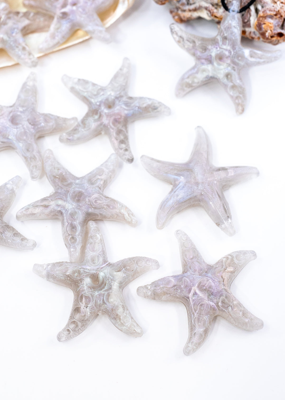 Several translucent starfish-shaped beads or pendants made from German resin arranged on a white background, with a small shell prop at the top.