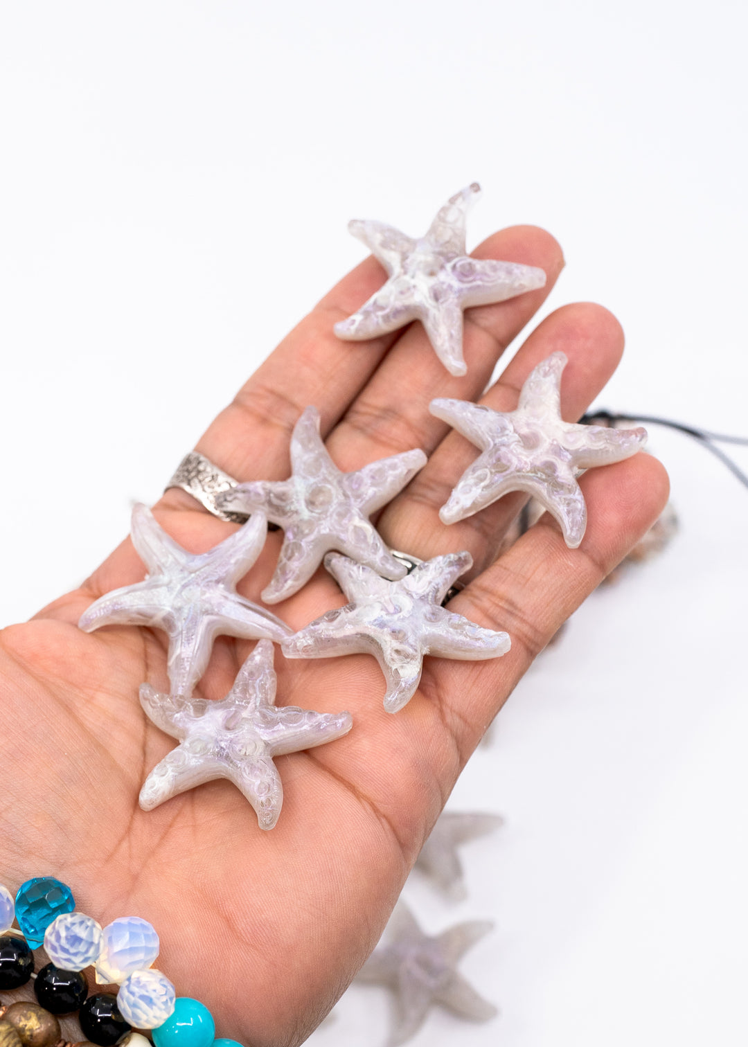A hand holding several translucent white starfish-shaped jewelry charms made from German resin or beads against a plain white background.