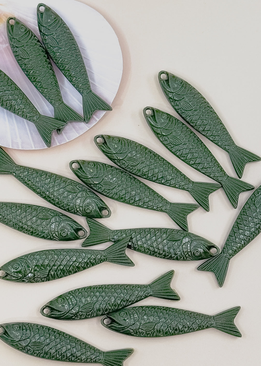 Multiple dark green fish-shaped jewelry charms with detailed scale engravings, sardine charms.