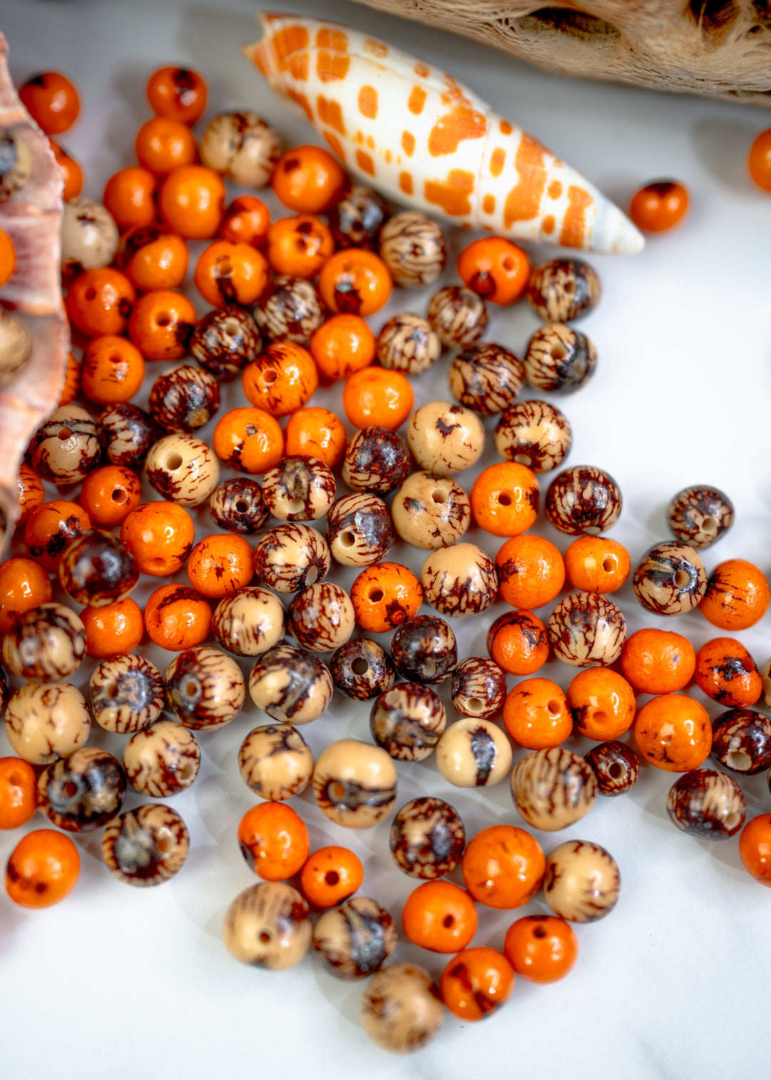 A collection of real Acai beads in orange, brown, and cream colors, with a natural pattern and black markings, displayed on a white surface.