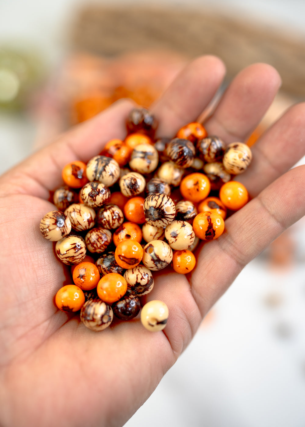 Brown and Orange Acai Beads Mix in the hands showing the different sizes of beads.