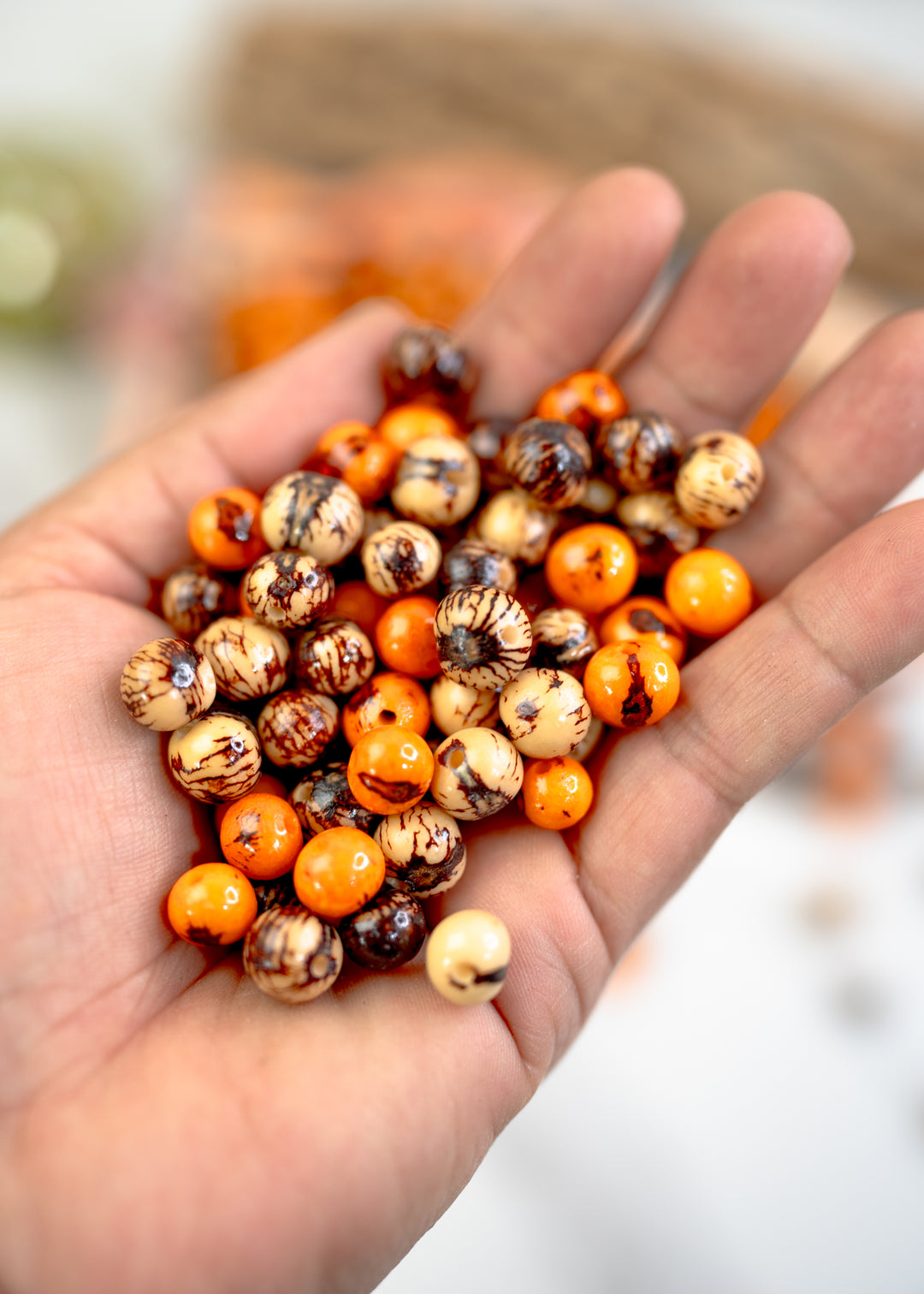 Brown and Orange Acai Beads Mix in the hands showing the different sizes of beads.