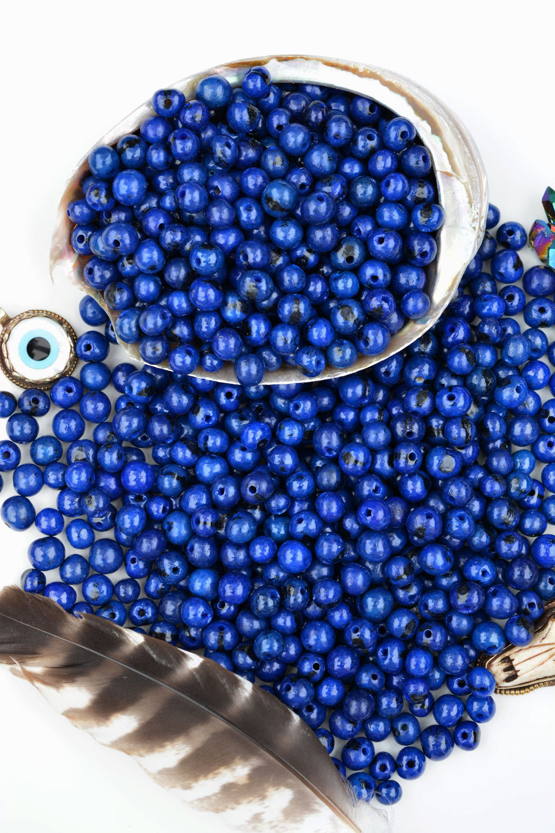 A collection of royal blue acai beads of varying sizes with a thin layer of varnish, alongside a feather and other beads.
