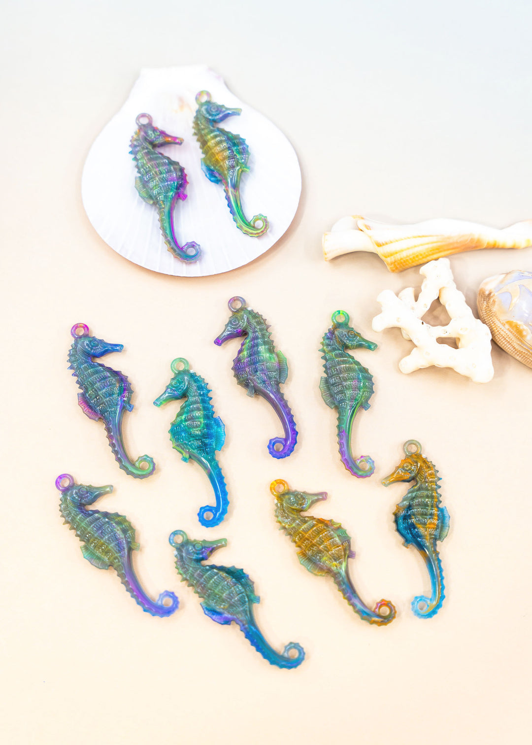 Colorful seahorse-shaped charms made from German resin on a white surface with shells in the background for jewelry making.
