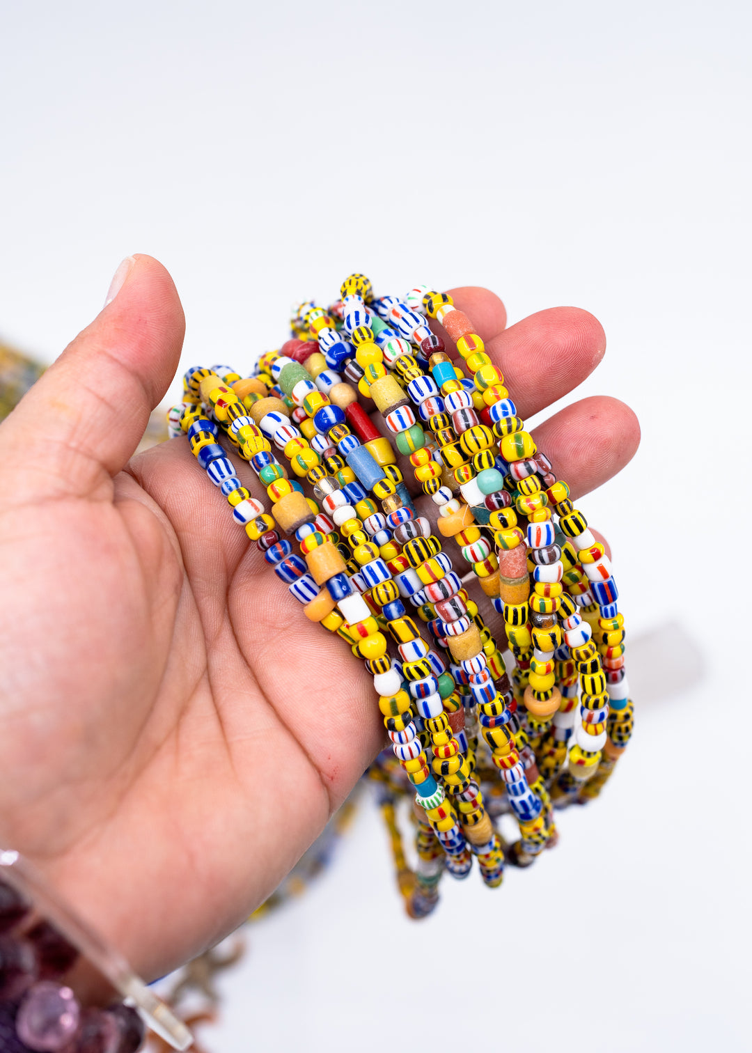 Showing a bunch of the Sunshine Confetti Ghana Glass Beads – Mixed Striped African Beads, 28 Inch Strand in the hand