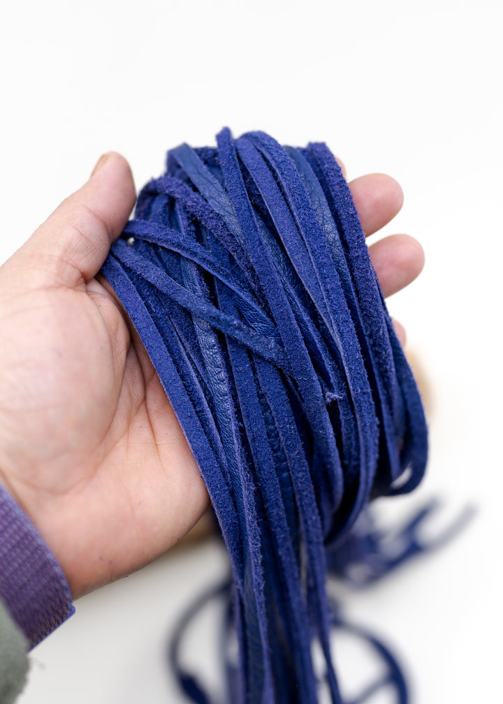 A hand holding a bundle of violet purple deef suede for jewelry making and crafts.