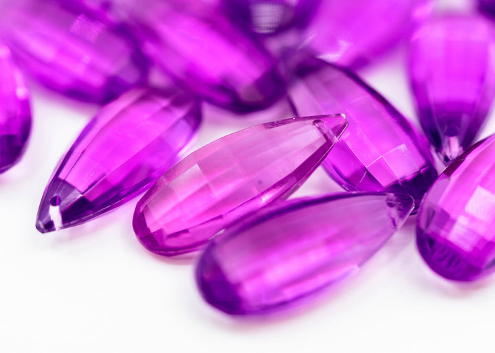 Faceted purple glass teardrop beads made from German resin scattered on a white background.