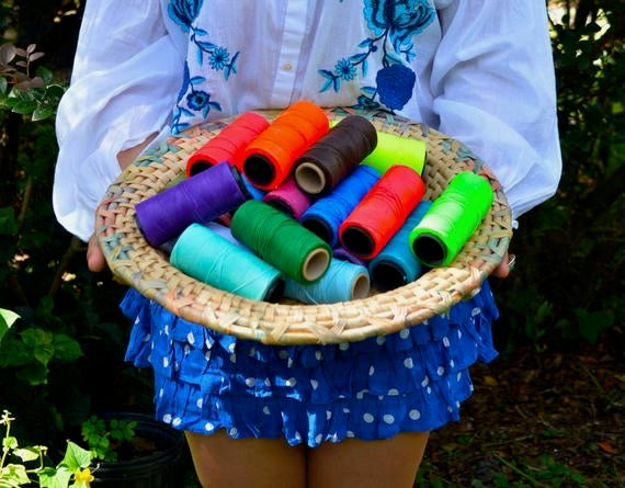 Person holding a woven basket filled with colorful spools of thread outdoors.