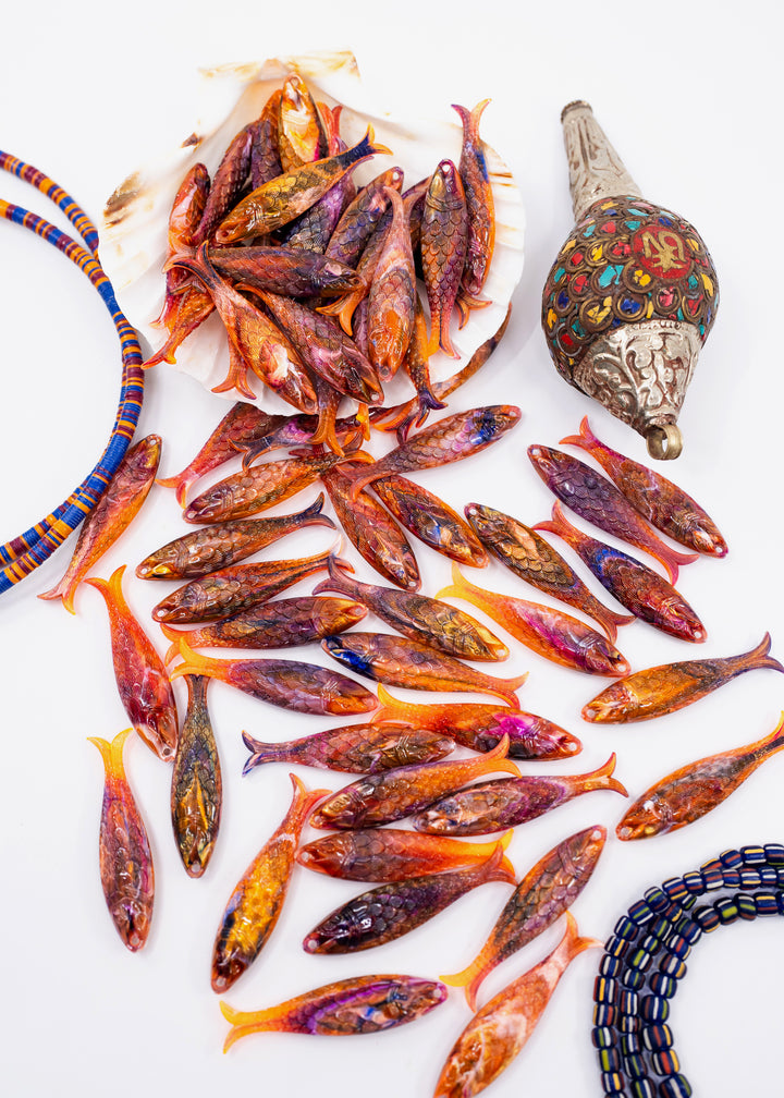 A collection of handcrafted German resin fish charms in vibrant orange, red, and purple tones, arranged on a white background alongside matching beaded jewelry.