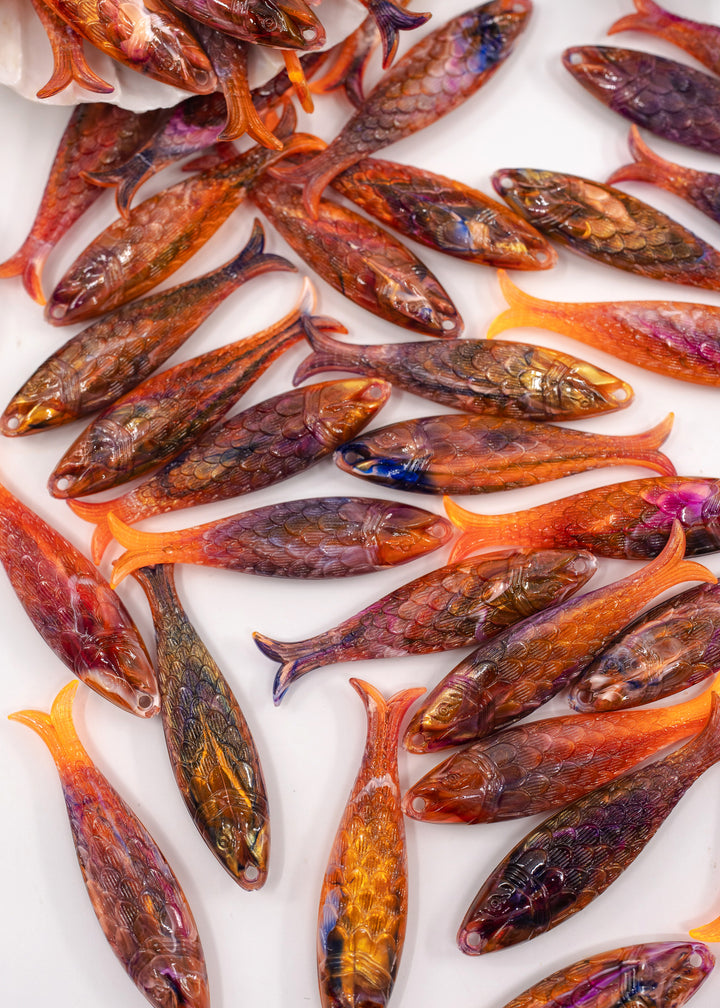 A collection of small, fish-shaped German resin beads with detailed scales and vibrant orange tails, arranged on a white background.