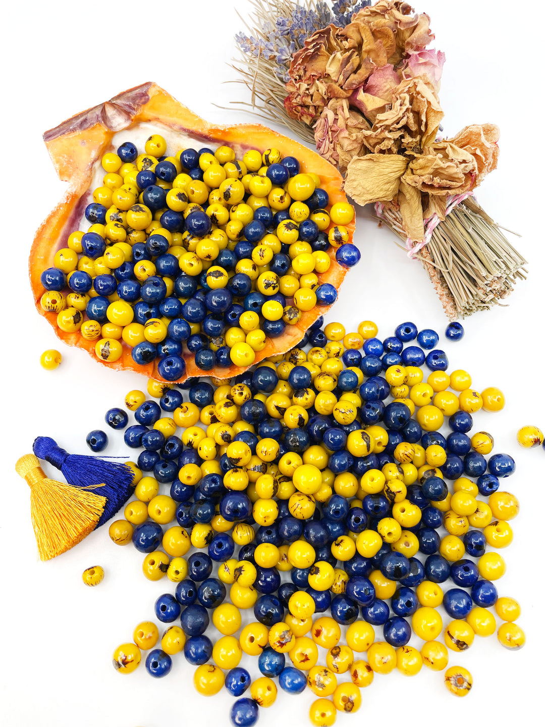 Blue and yellow Acai Beads displayed with tassels and a bundle of sage.