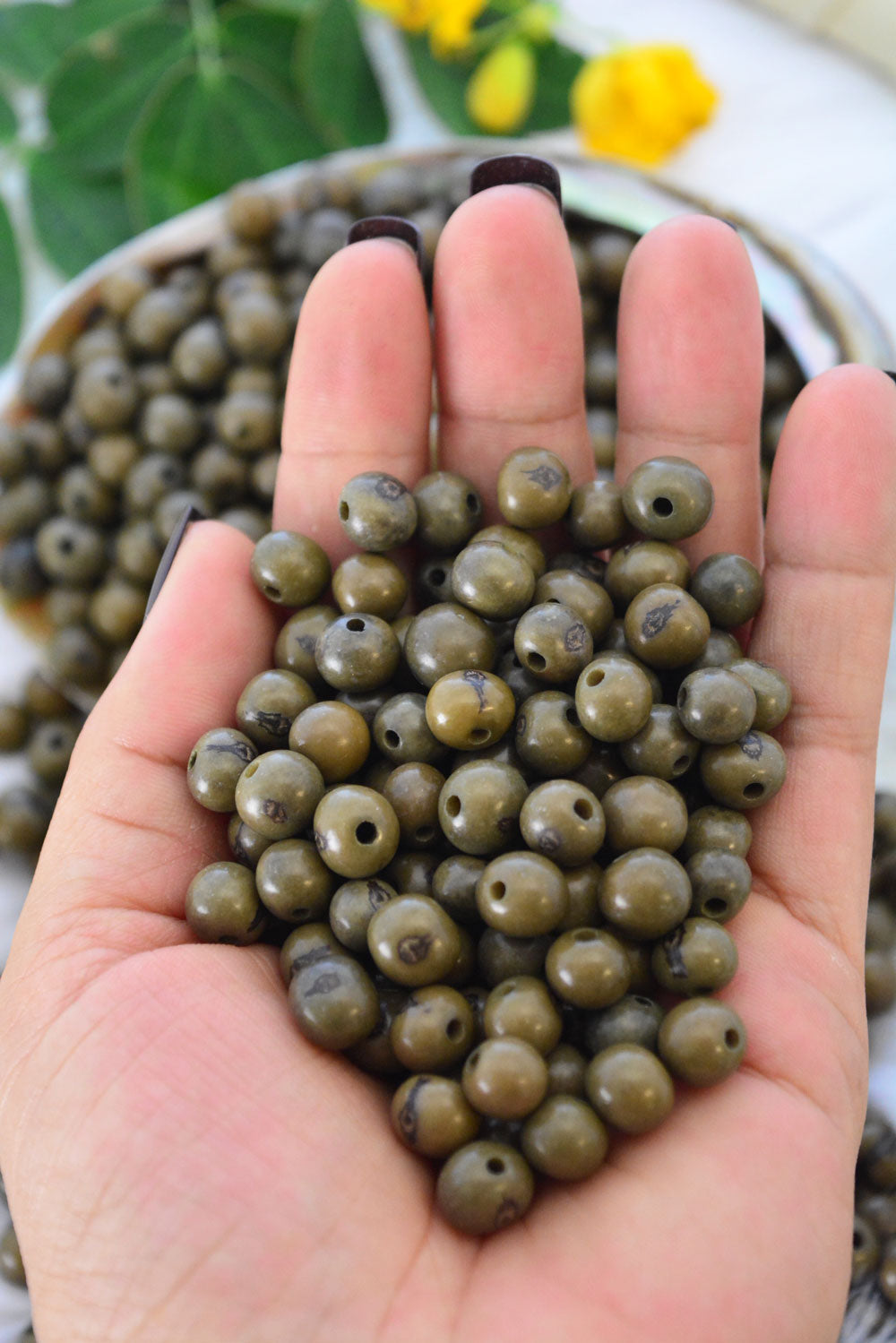 Dark Olive Green Acai Beads close-up in the hands showing the different bead sizes.