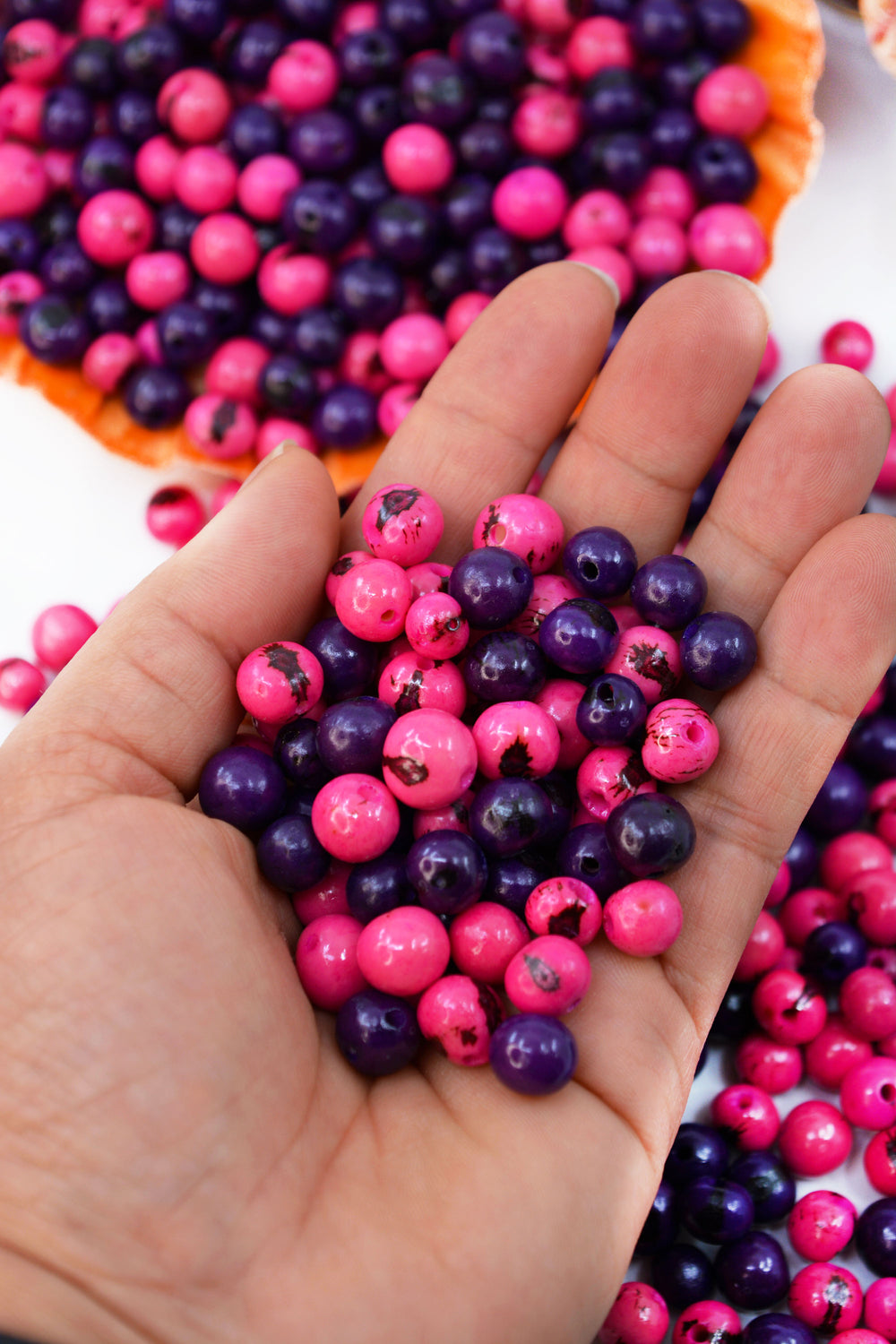 A close-up of Electric Love, Pink and Purple Acai Beads in the hands showing the variance in size.