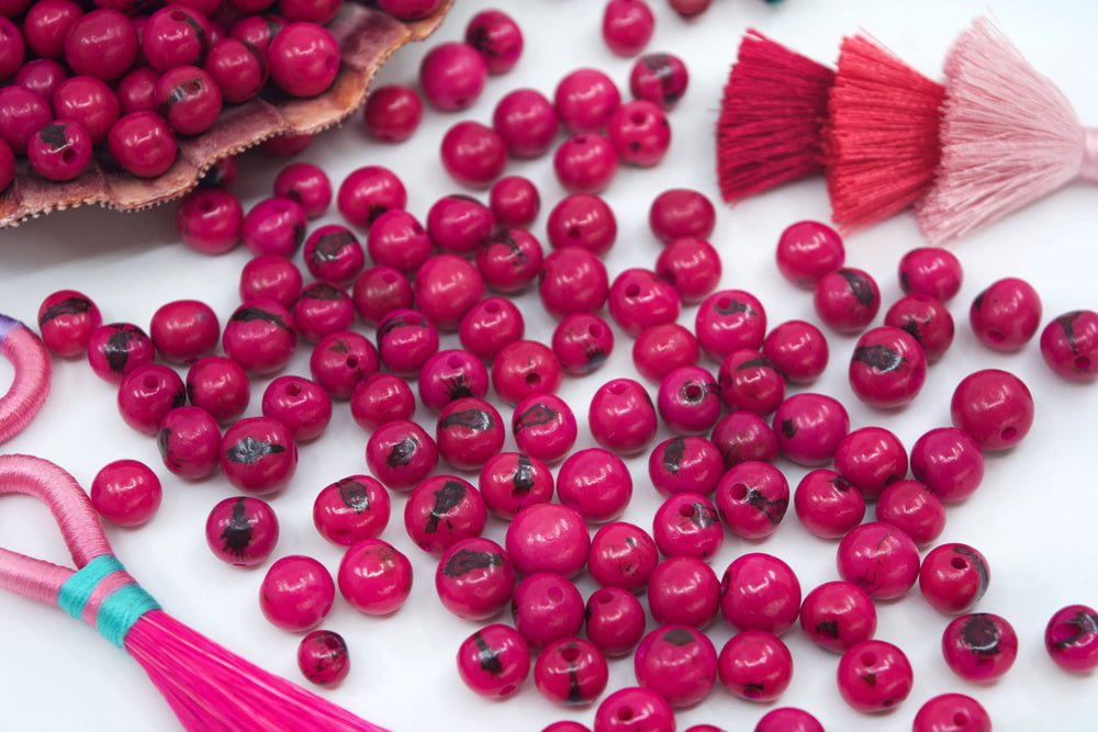 Fuchsia Pink Acai Beads showing the size of the holes and variance in size of the beads.