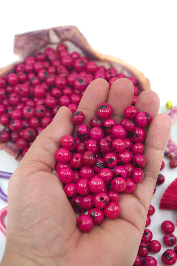 Fuchsia Pink Acai Beads close-up in the hands.