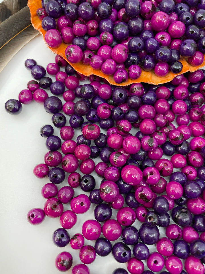 An assortment of purple acai beads in a white background showcasing the variance in natural bead sizes.