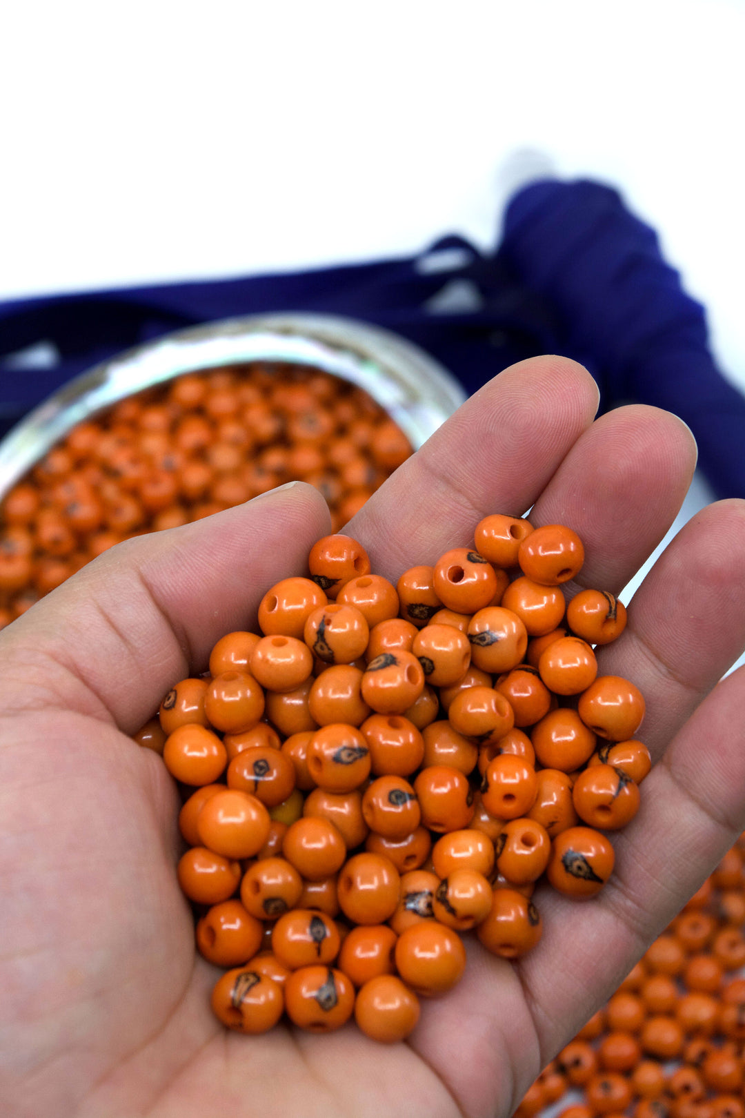 Close-up of orange acai beads in the hands showing the size of the beads.