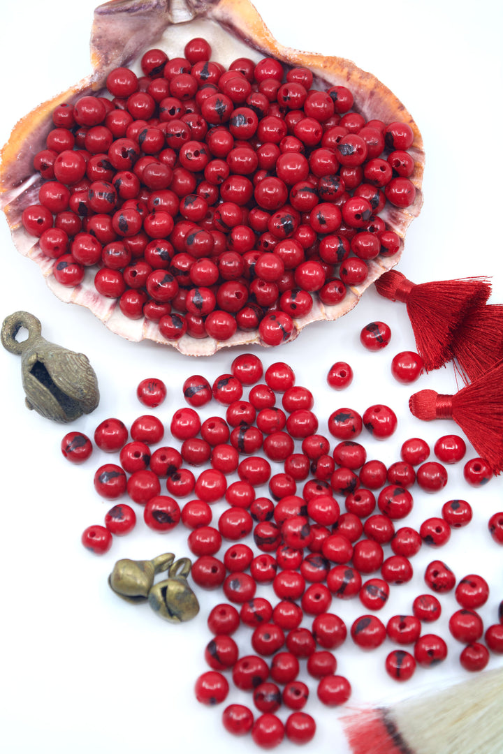 Scarlet Red Acai Beads displayed on a seashell for jewelry making.