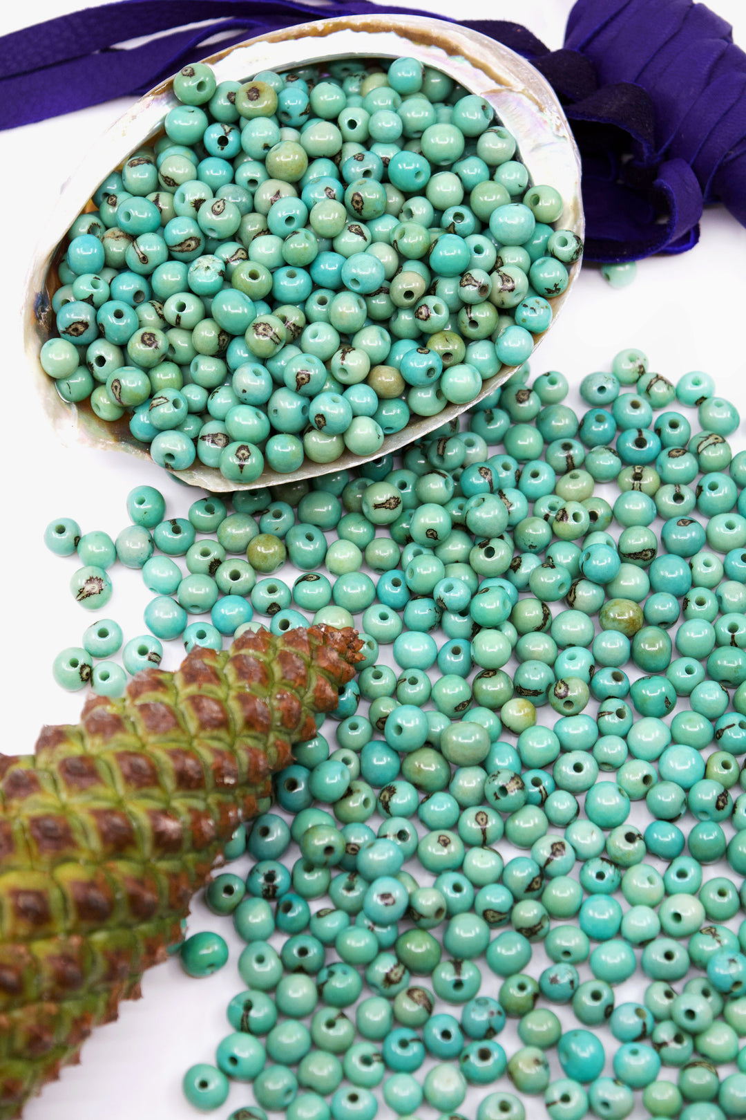 A collection of sea foam blue acai beads, with varying shades of blue and natural patterns, hand-drilled and displayed on a reed.