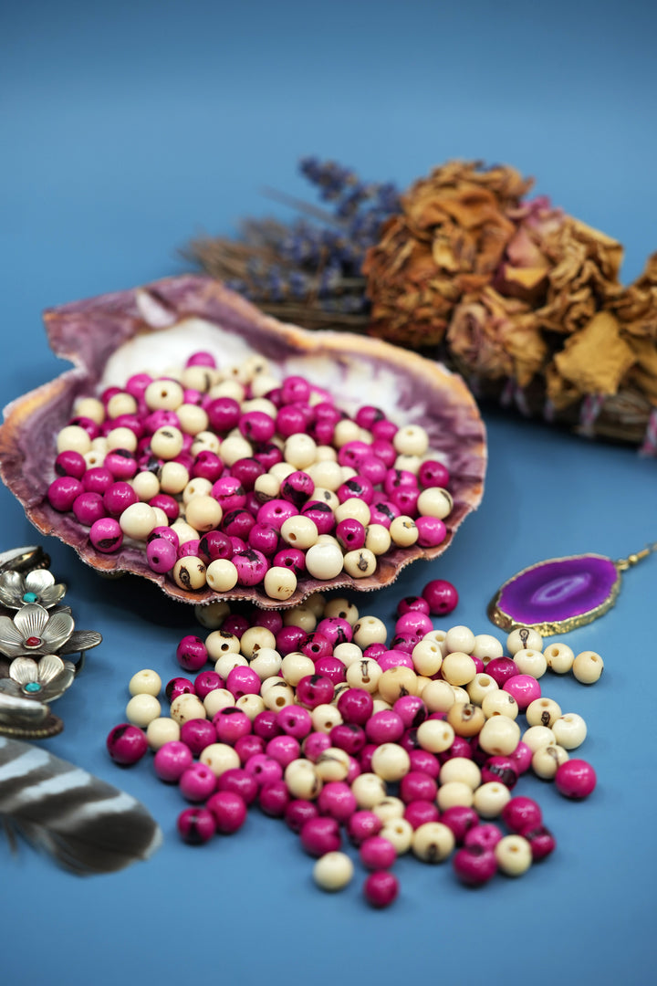 A beautiful assortment of Pink and White Acai Beads displayed in a blue background with beads in a seashell.